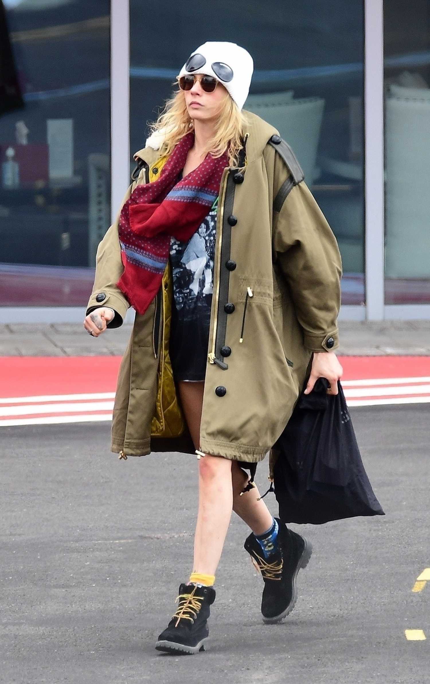 Cara Delevingne in a White Beanie Hat Arrives at Battersea Helipad in